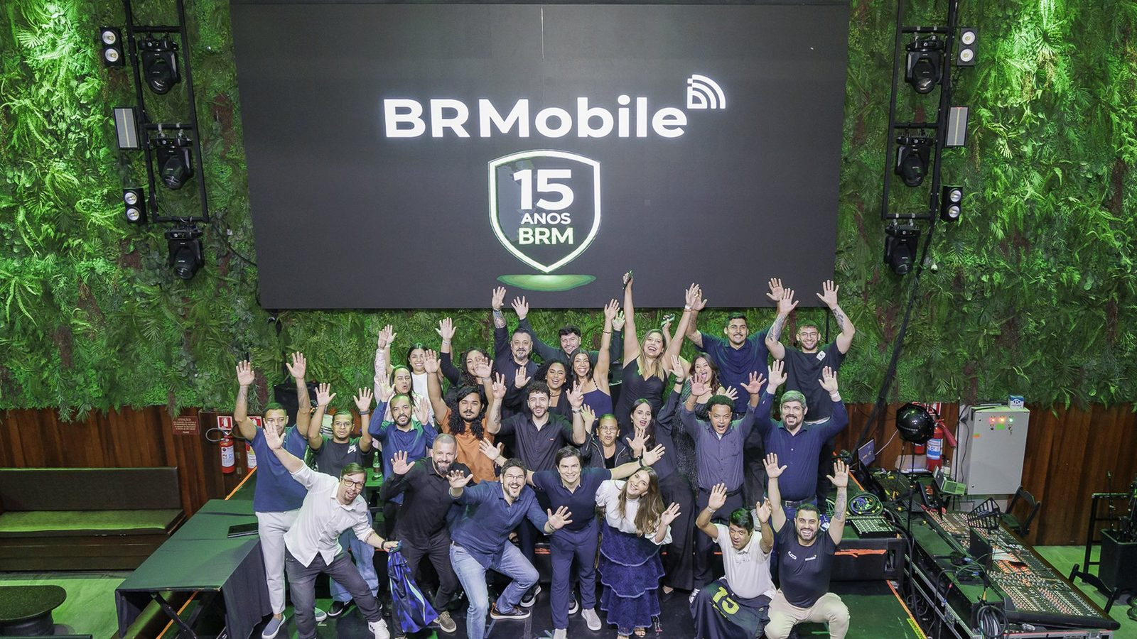 Equipe celebrando o aniversário de 15 anos da BR Mobile diante do painel comemorativo